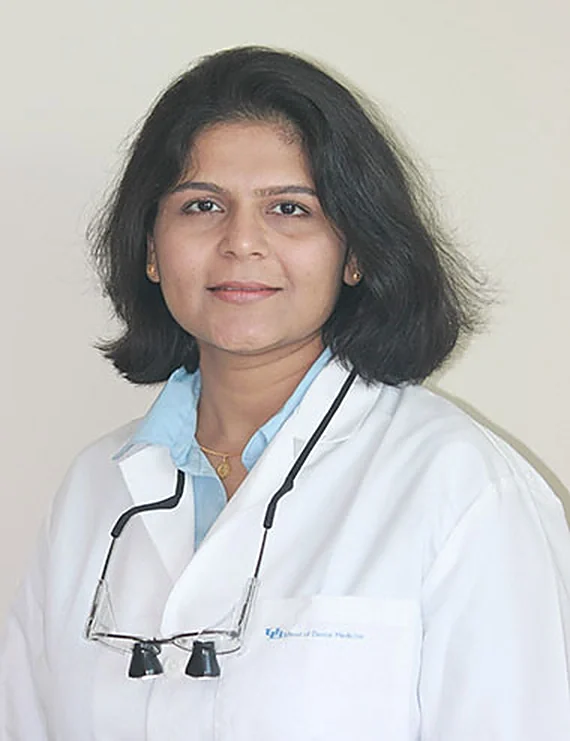 Dr. Kunjal Patel, DDS, in a white coat with dental loupes.