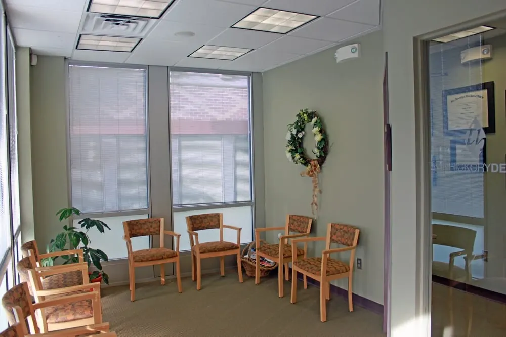 The waiting room at Twin Hickory Dental, with wooden chairs by tall windows.